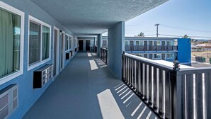 A long, narrow corridor with a balcony on one side, leading to a door at the end. - Motel 6 Ridgecrest, CA - China Lake (Ridgecrest)