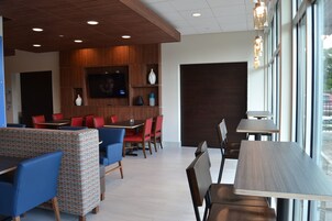 Interior moderno de restaurante con paneles de madera, televisor de pantalla plana, asientos en rojo y azul, y ventanas amplias.