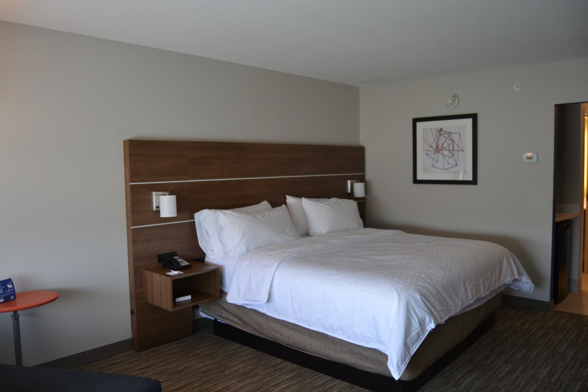 A hotel room with a large bed, a bedside table with a phone, a nightstand, and a framed picture on the wall.