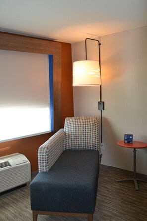 A small, single-bed room with a checkered bed, a standing lamp, a small table, and a window with blinds. - Holiday Inn Express & Suites Goodlettsville N - Nashville by IHG (Goodlettsville)