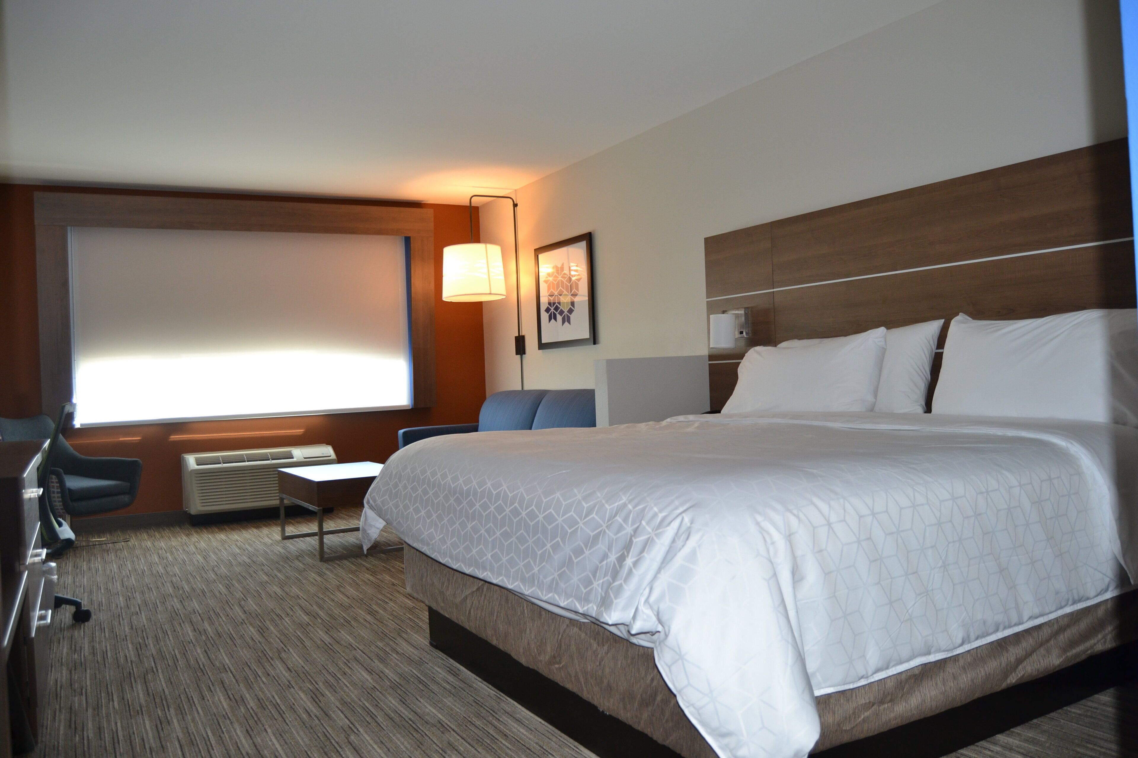 A hotel room with a large bed, a desk, a chair, a flat-screen TV, and a wall-mounted lamp.