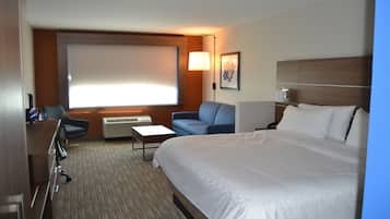 Une chambre d’hôtel avec un grand lit, un bureau, une chaise, un canapé, une télévision et une fenêtre avec des stores.