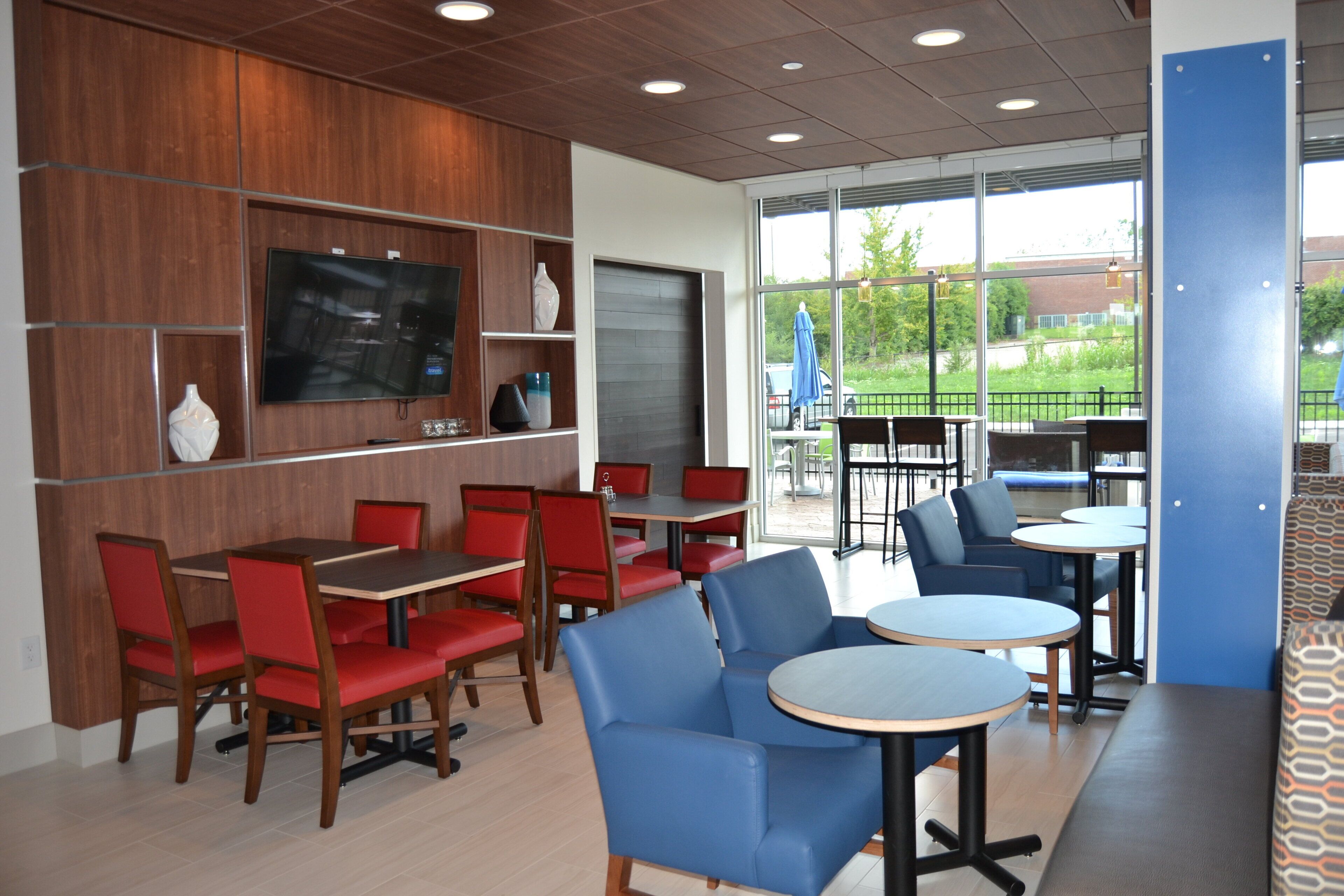 Interior de un restaurante con paredes de paneles de madera, un televisor de pantalla plana, asientos en rojo y azul, y ventanas amplias que ofrecen vista al exterior.