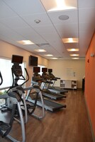Un gimnasio con cintas de correr, un televisor en la pared y un cartel que indica el uso del espacio.