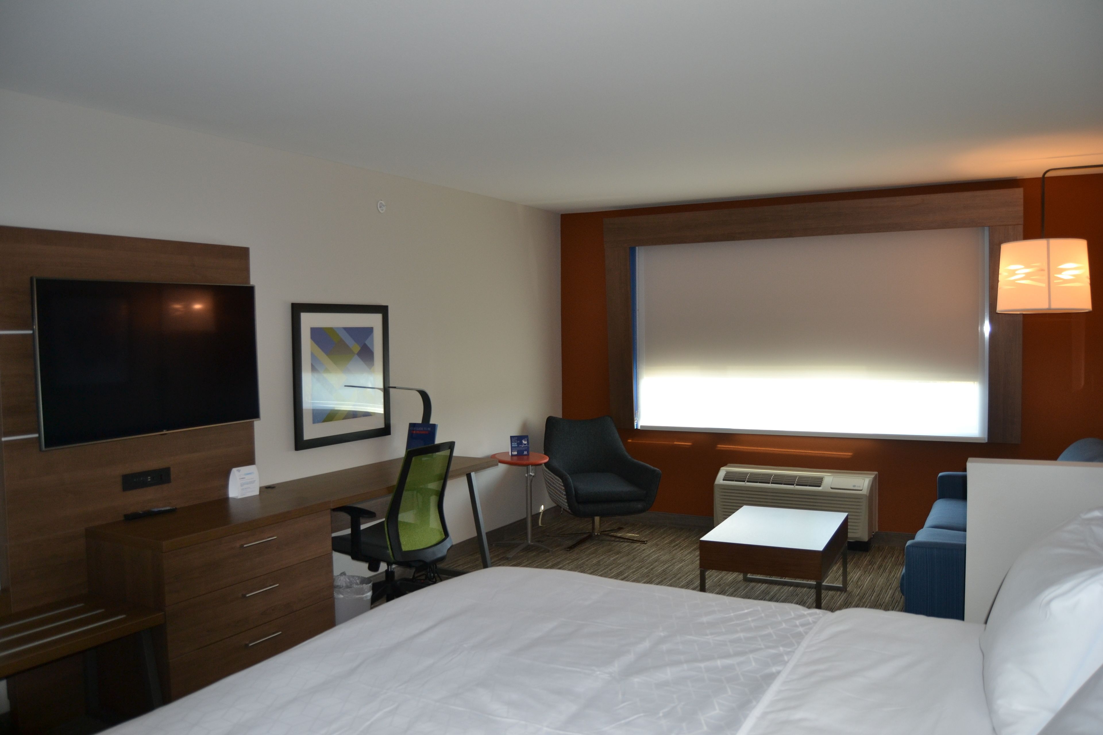 A hotel room with a bed, a desk, a chair, a TV, and a large window.