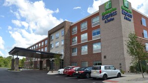 Ein Holiday Inn Express & Suites Gebäude mit Backsteinfassade, zahlreichen Fenstern und einem überdachten Parkbereich mit mehreren Autos.