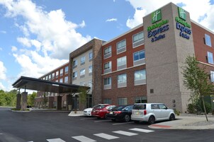 Edificio de Holiday Inn Express & Suites con fachada de ladrillo, múltiples ventanas y un área de estacionamiento techada con varios automóviles.