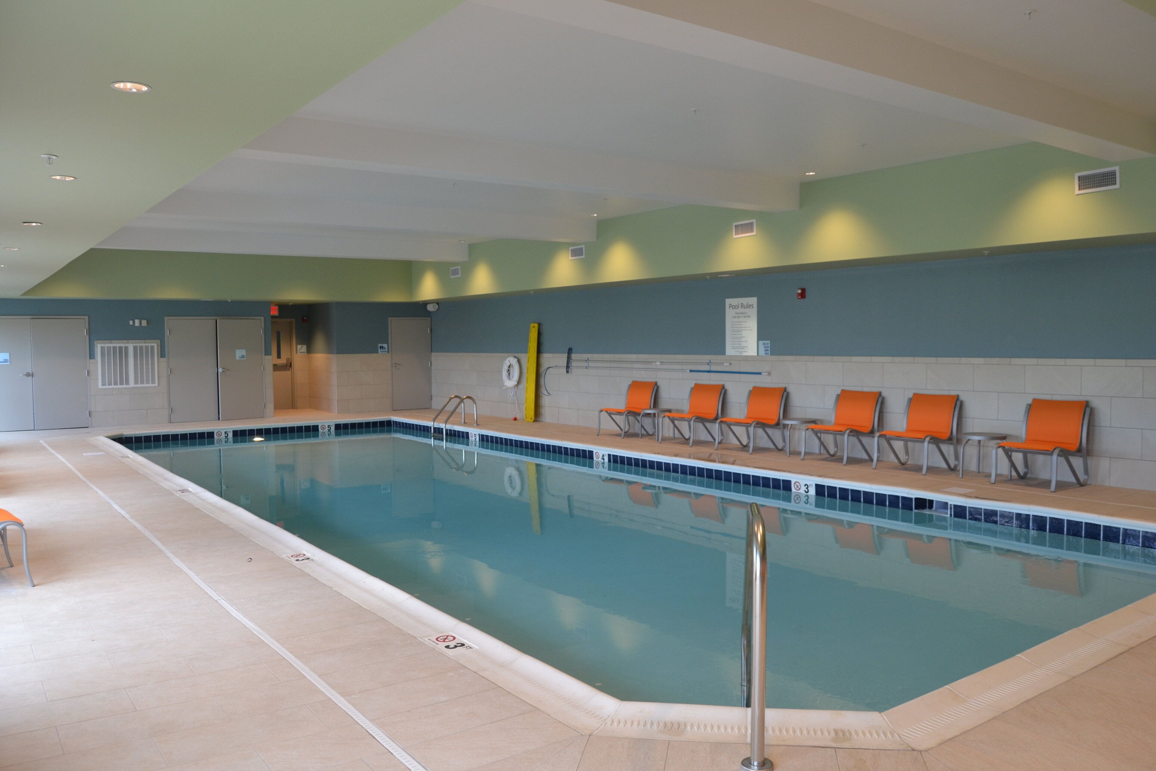 A swimming pool with a tiled edge, a pool ladder, and several orange chairs along the side.