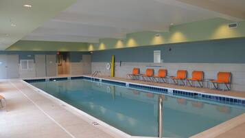 A swimming pool with a tiled edge, a pool ladder, and several orange chairs along the side.