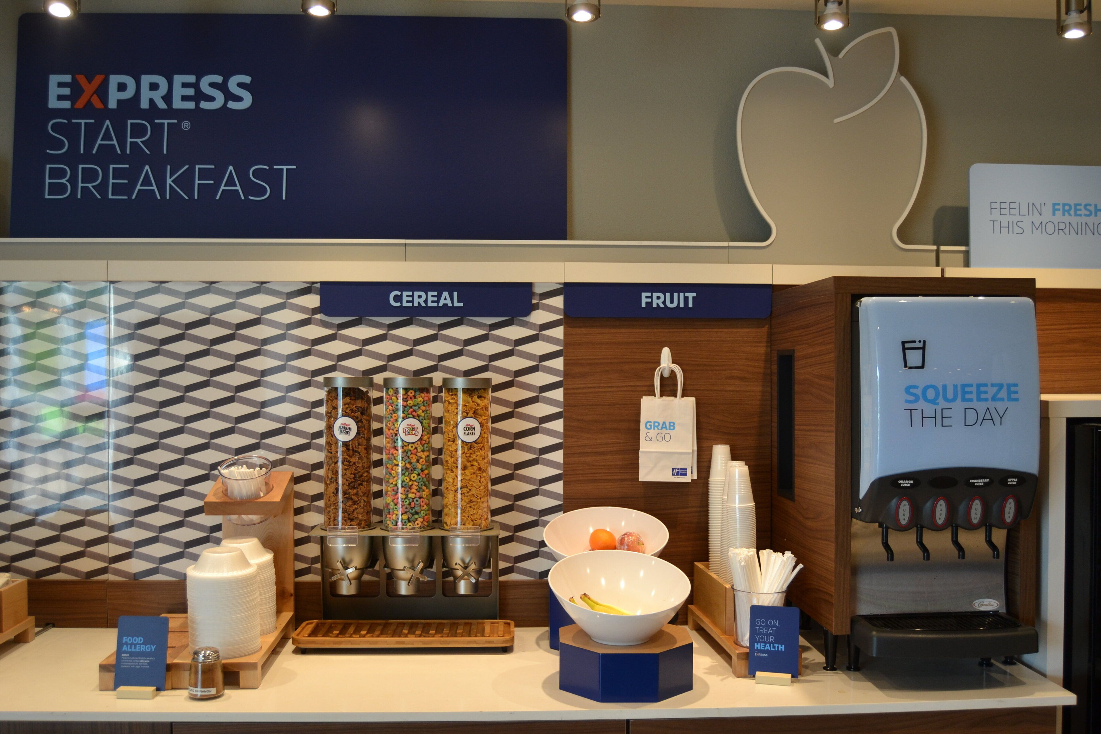 A breakfast area with labeled sections for cereal and fruit, a beverage dispenser, and a sign indicating a health-focused message.