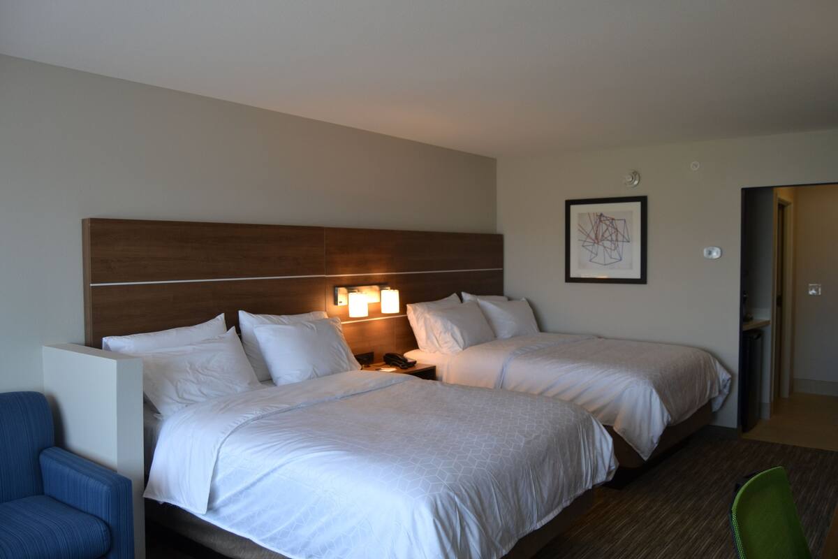 A hotel room with two beds, a nightstand, a chair, and a framed picture on the wall.