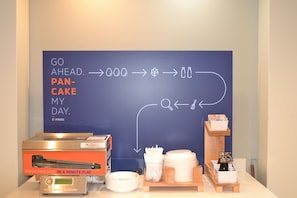 Ein Frühstücksbuffet mit Grillplatte, Tellern, Servietten und einer Kaffeestation.