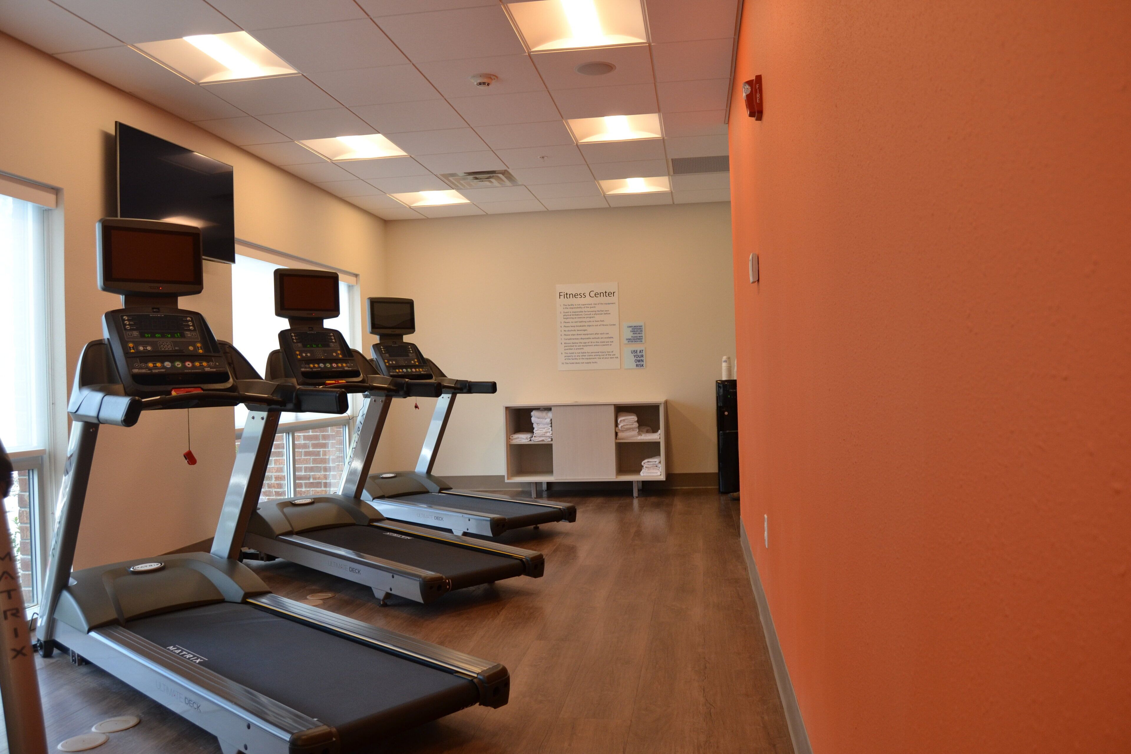 Un gimnasio con cintas de correr, una pantalla en la pared y un cartel que indica el propósito del centro.