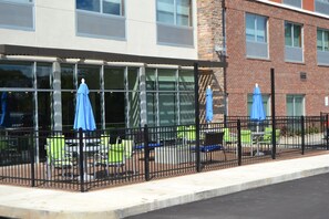 A building with large windows, outdoor seating with blue umbrellas, and a brick facade. - Holiday Inn Express & Suites Goodlettsville N - Nashville by IHG (Goodlettsville)