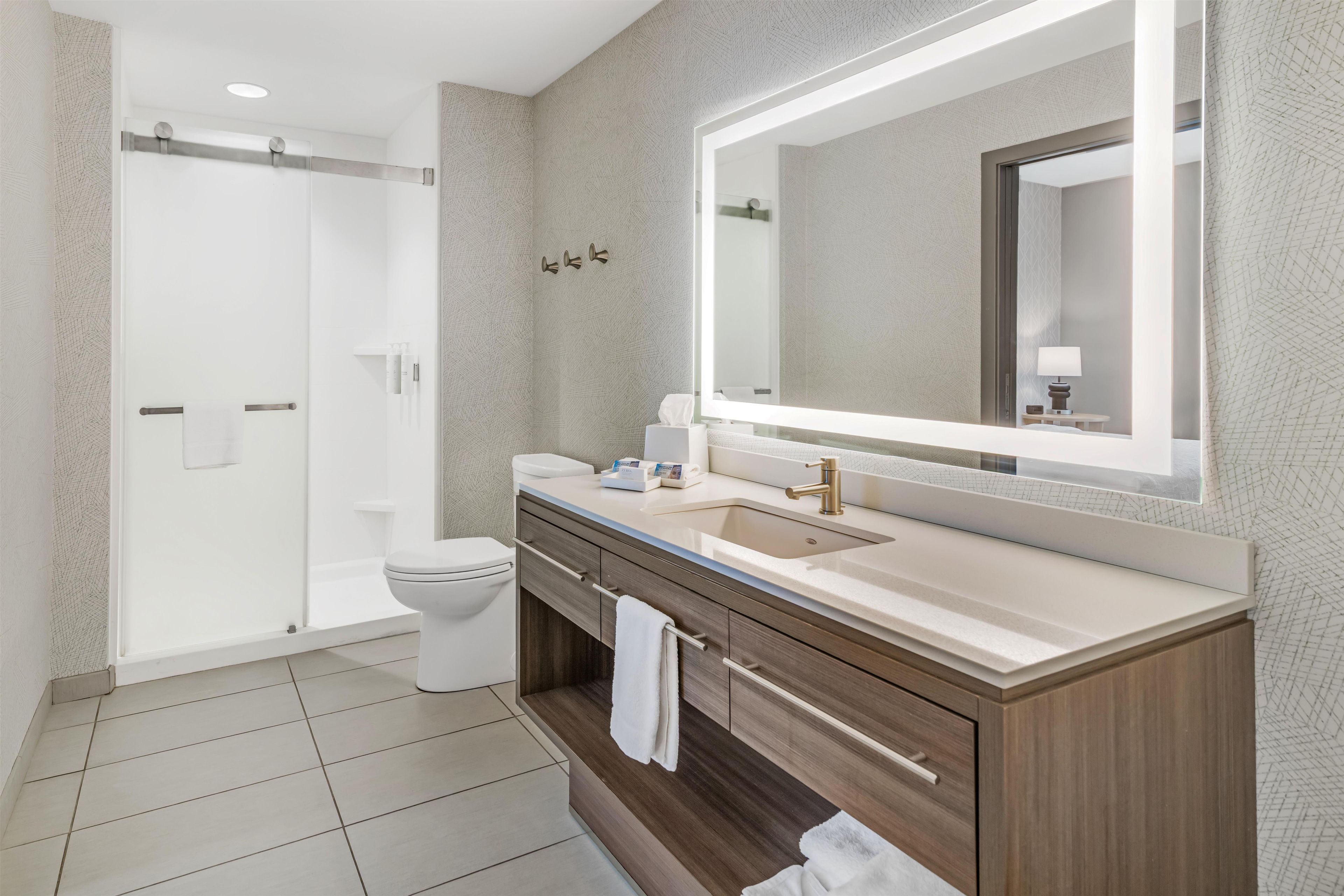 Un bagno moderno con doccia a filo pavimento, un WC, un lavandino con un ampio specchio e mobili in legno.