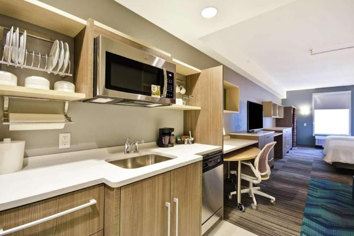Een moderne hotelkamer met een kitchenette, een bureau, een stoel, een bed en een raam.