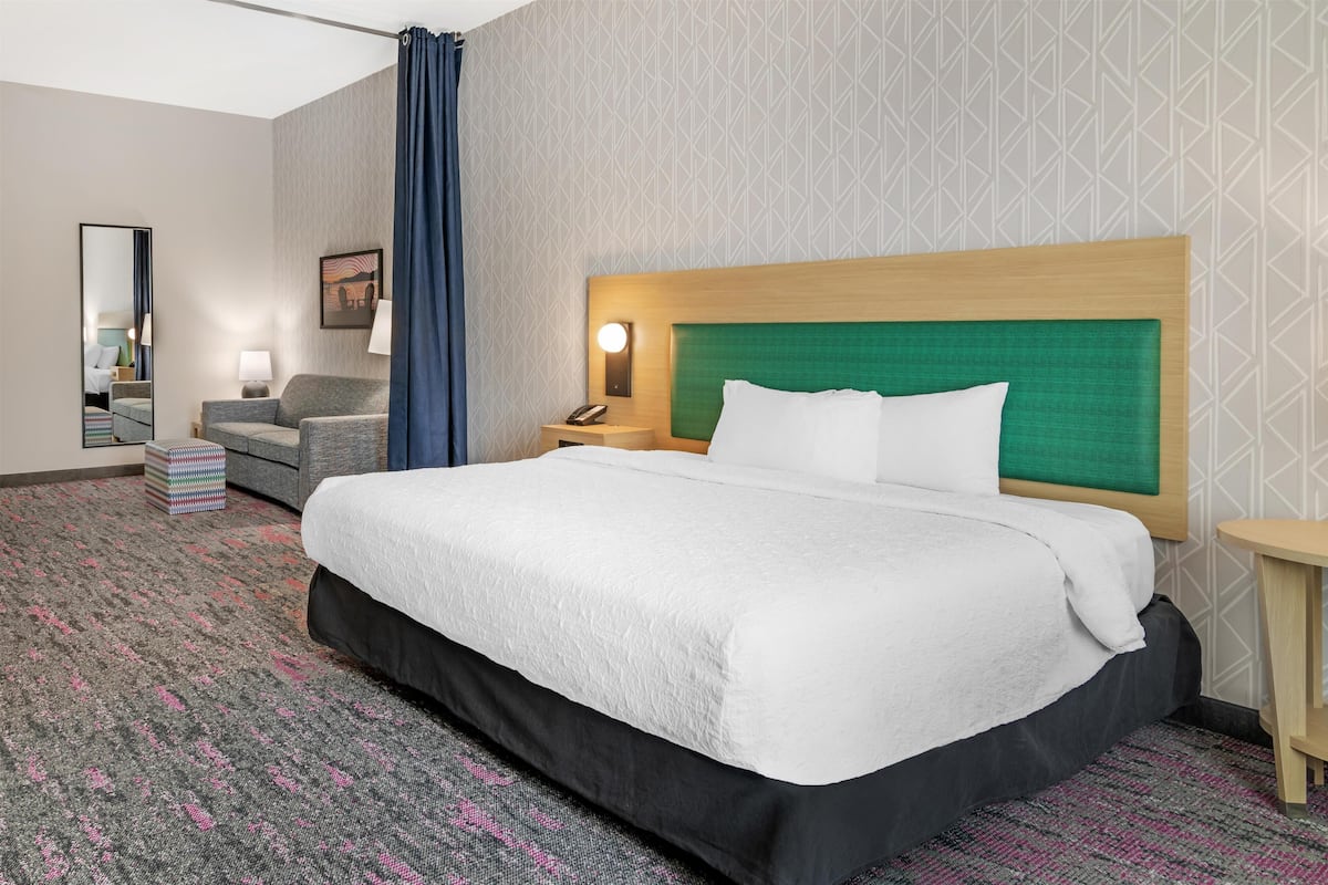 Hotelkamer met een groot bed, een bureau, een stoel, een nachtkastje, een lamp, een spiegel en een kamerbreed tapijt met patroon.