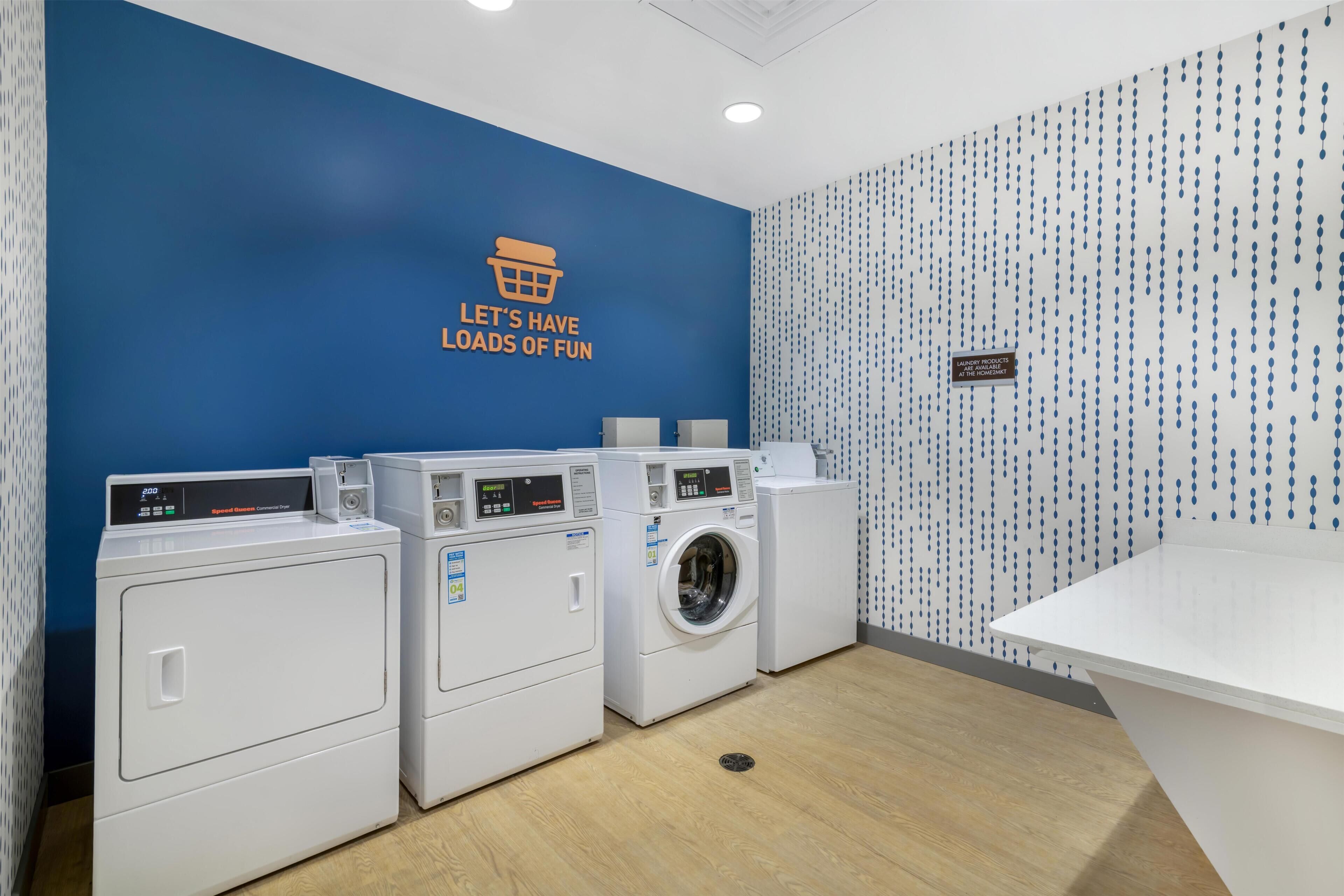 A laundry room with three white washing machines and a blue wall with a motivational quote.