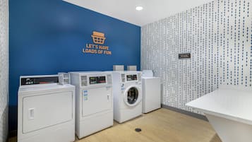 A laundry room with three white washing machines and a blue wall with a motivational quote.