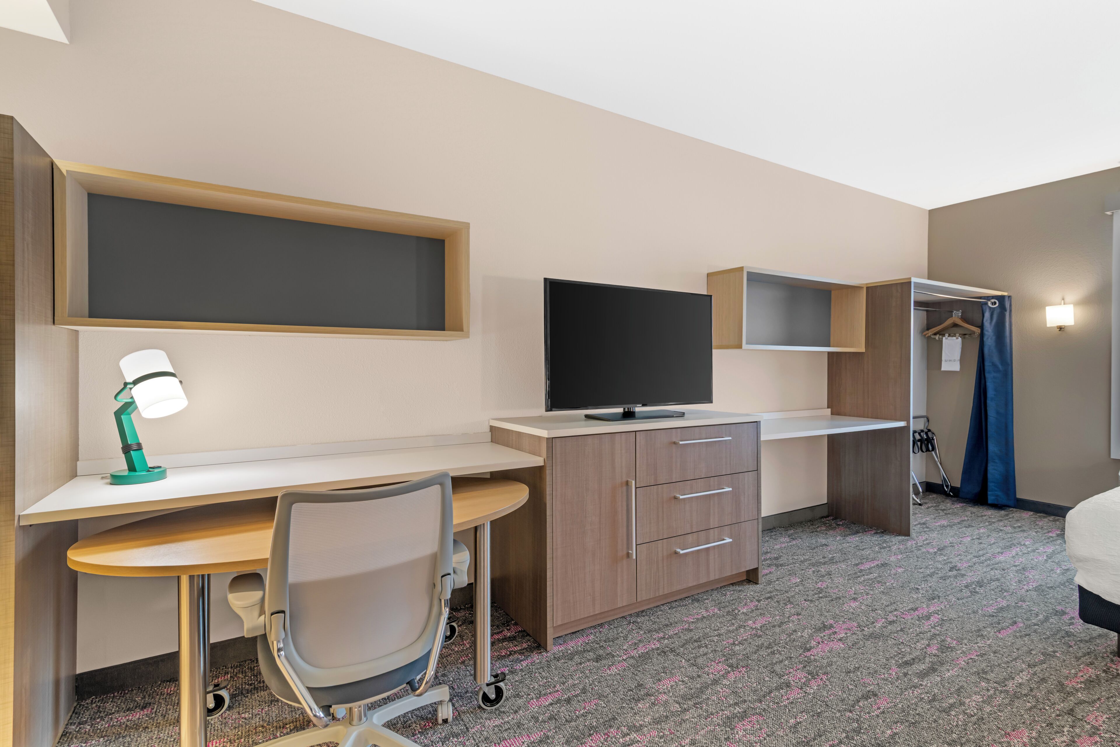 Habitación de hotel con escritorio, silla, televisión, armario y zona de ducha.