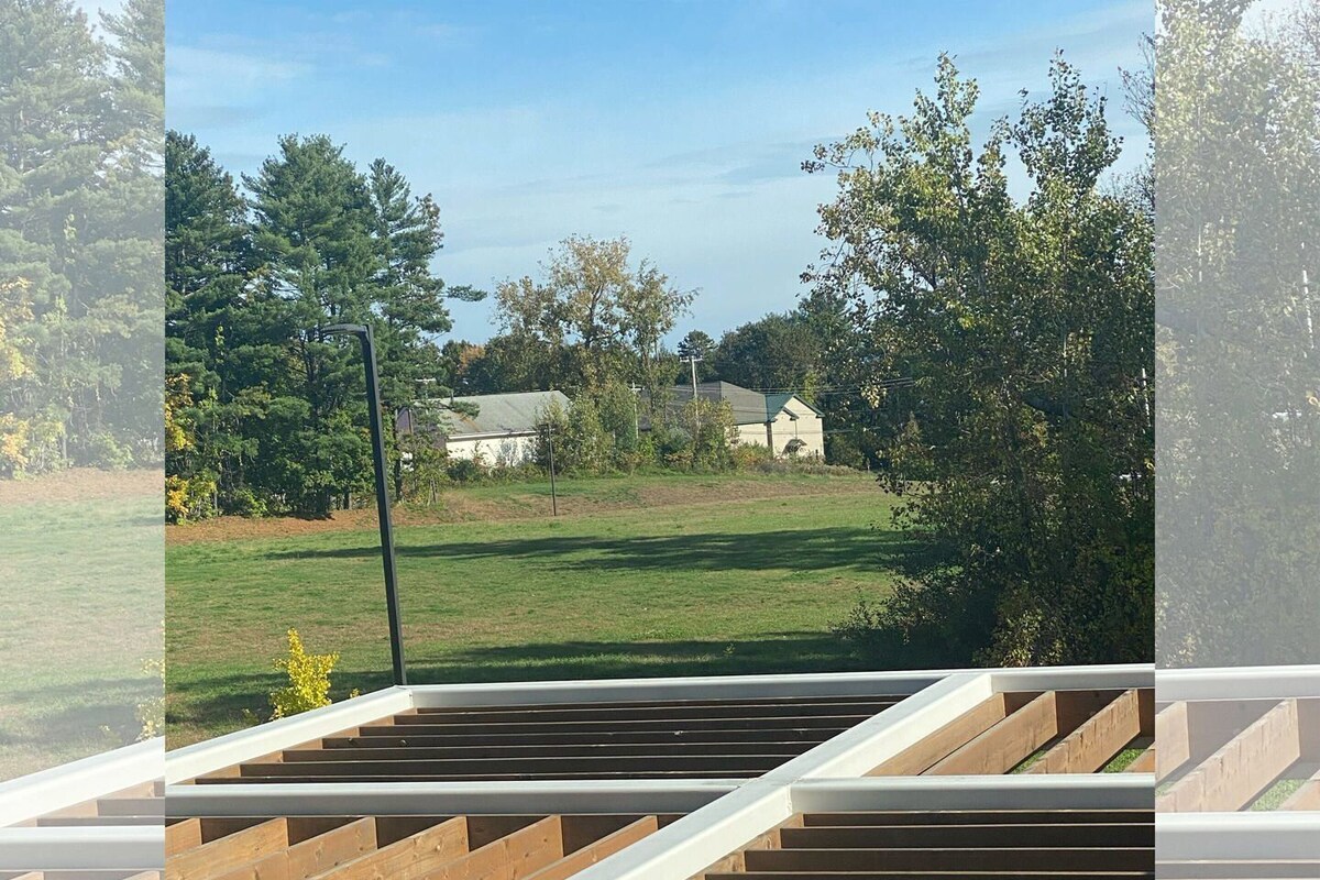 Uitzicht vanuit een raam, met een houten terras, een grasveld en huizen op de achtergrond.