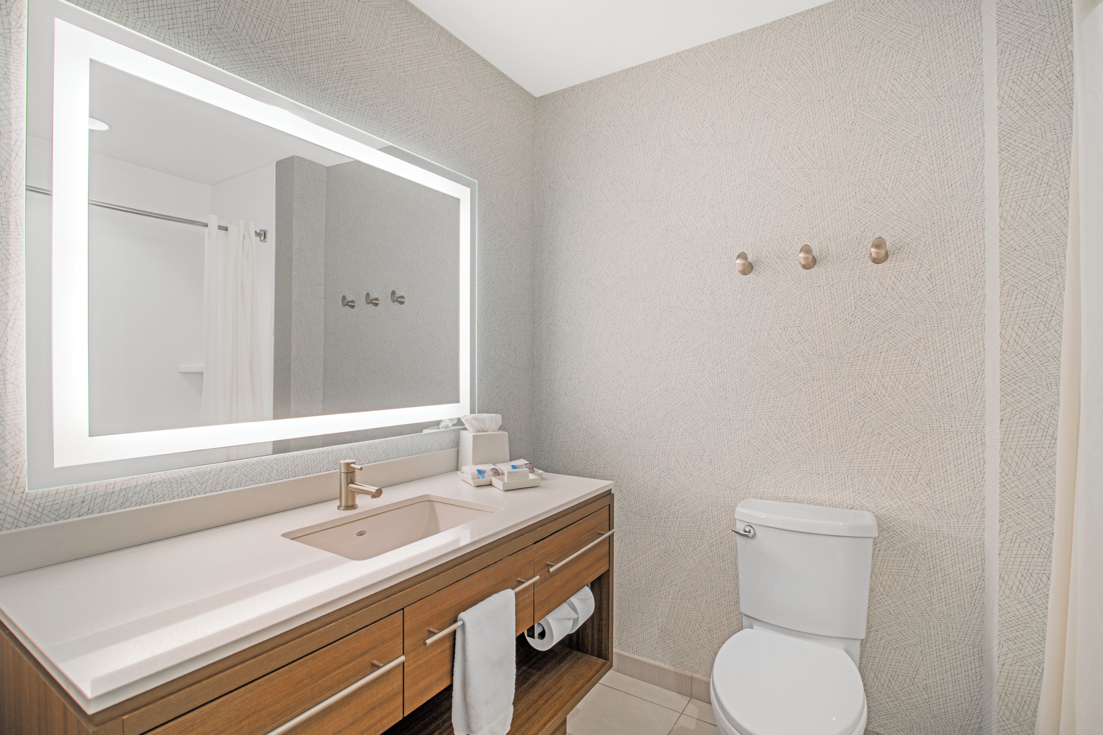 A bathroom with a large mirror, a sink, a toilet, and a towel rack.