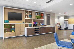 A modern kitchen area with a flat-screen TV, built-in cabinets, and a coffee station. - Home2 Suites by Hilton Queensbury Lake George (Queensbury)