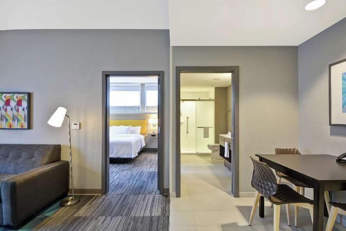 Een hotelkamer met een bed, een bureau, een stoel, een lamp en een badkamer zichtbaar door een open deur.