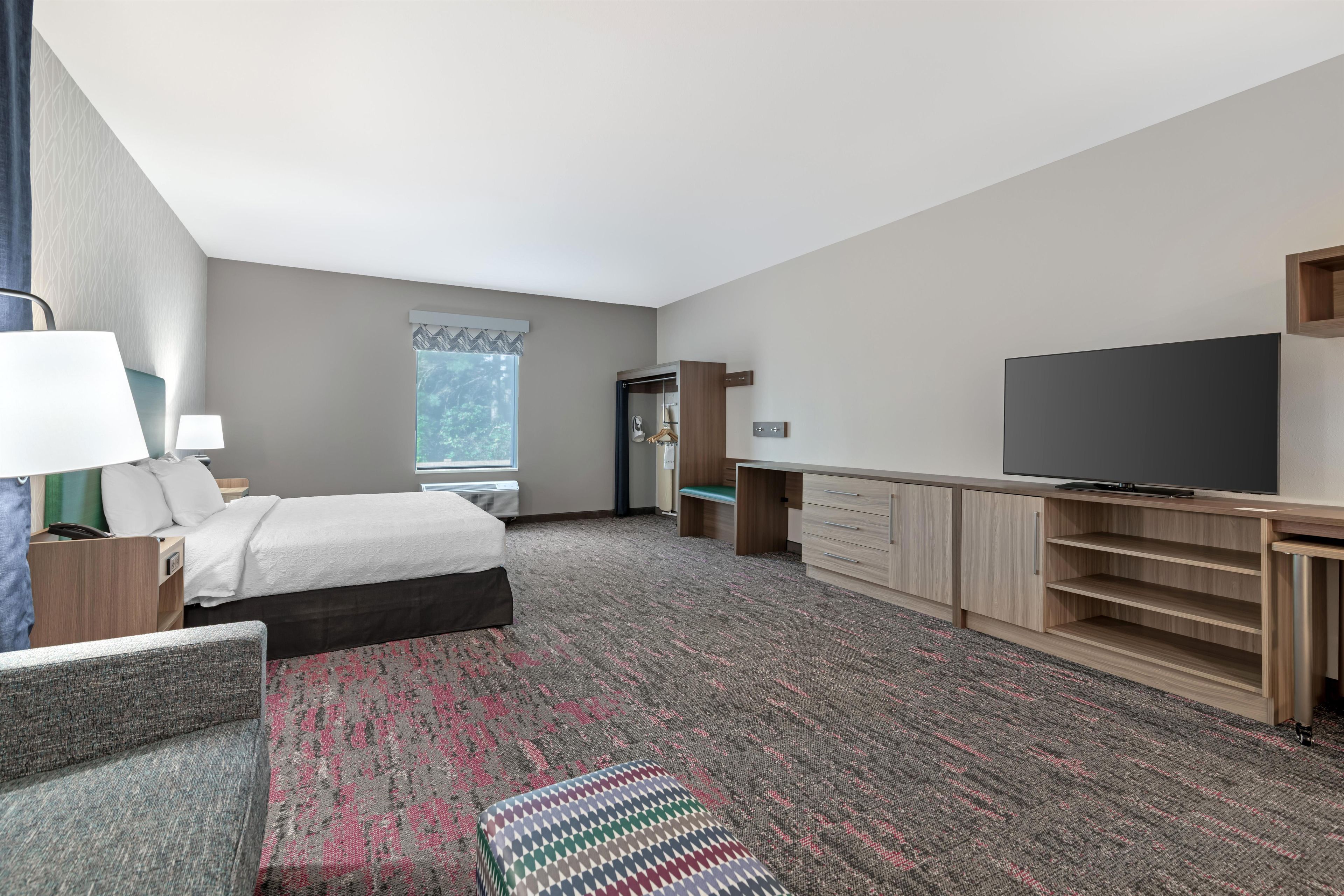 A hotel room with a bed, a desk, a television, and a window.