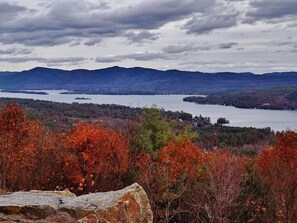 Een panoramisch uitzicht op een meer, omringd door bergen en herfstbomen.