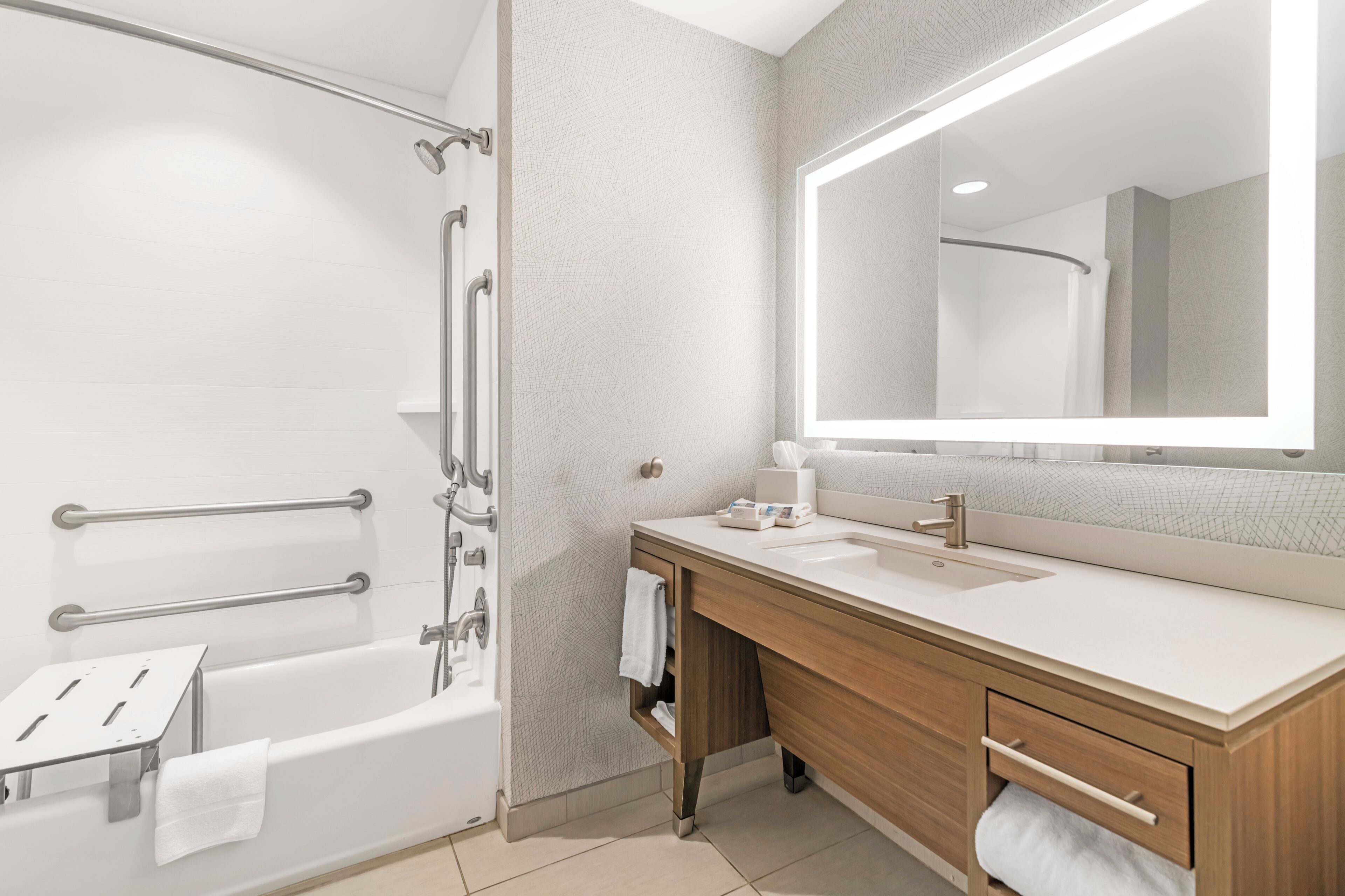 A modern bathroom with a bathtub, a large mirror, a sink, and a vanity.