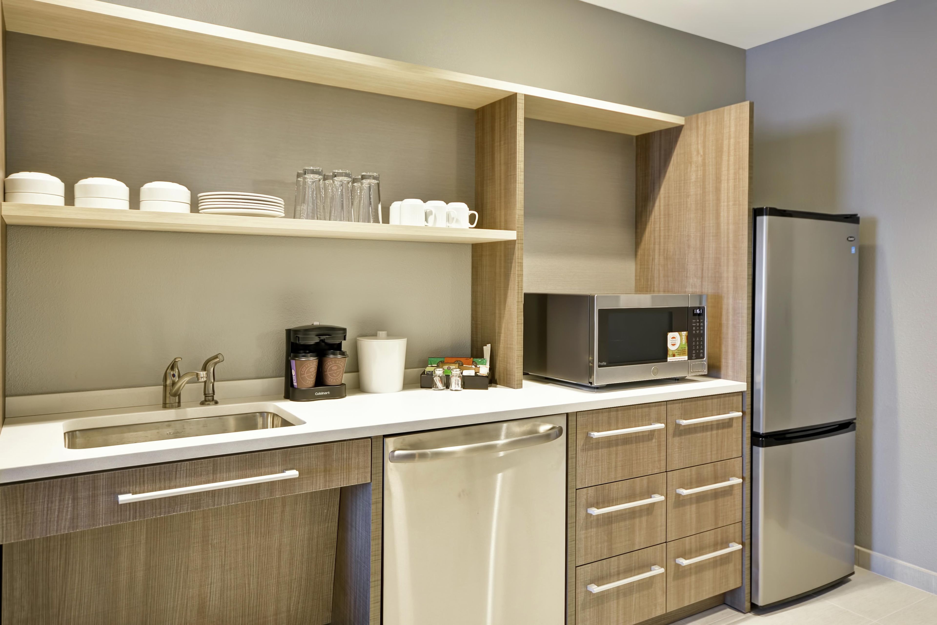 A modern kitchen with a stainless steel refrigerator, a microwave, a sink, and wooden cabinetry.