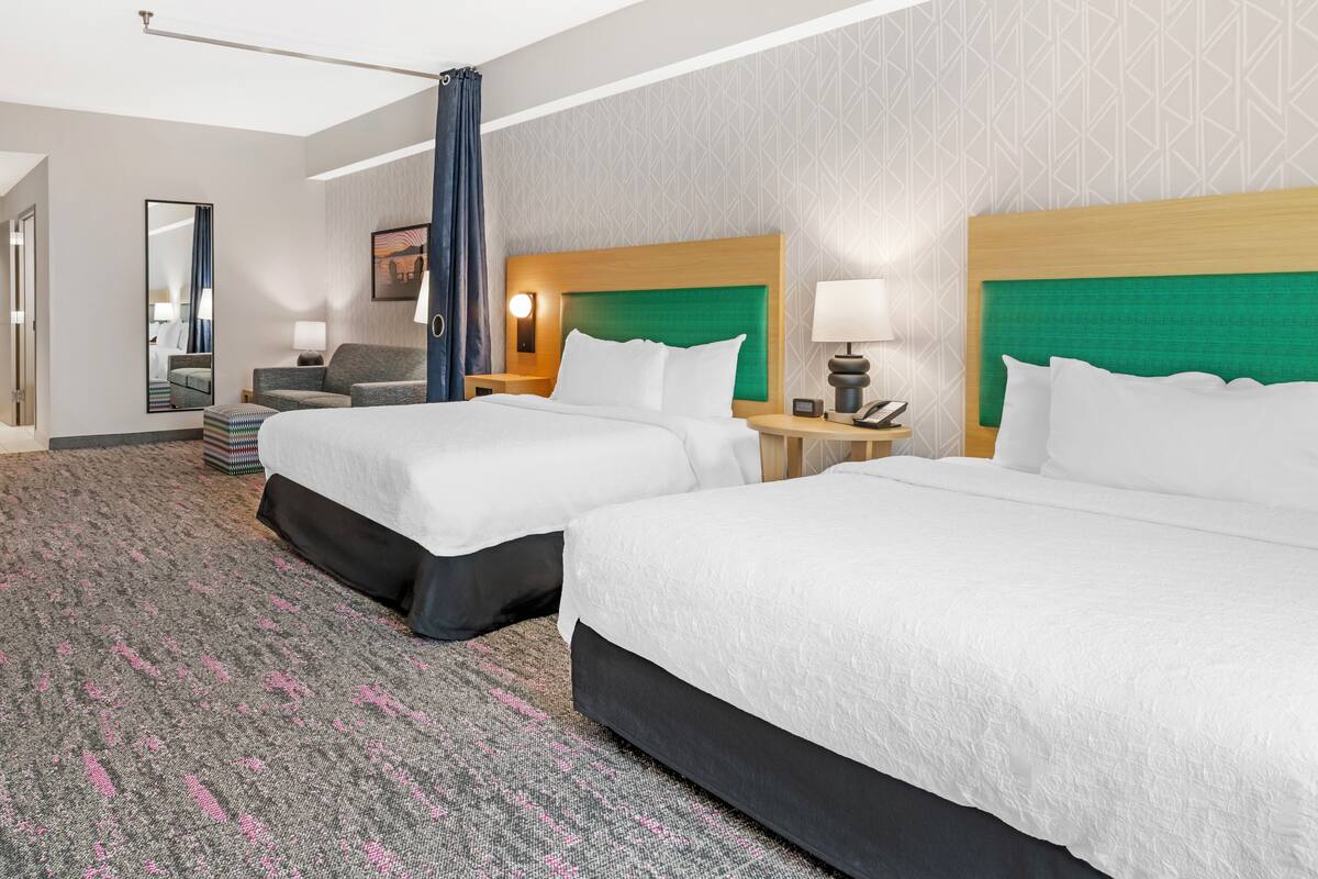 Een hotelkamer met twee bedden, een bureau, een stoel, een spiegel en een kamerbreed tapijt met een patroon.