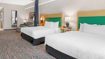A hotel room with two beds, a desk, a chair, a mirror, and a patterned carpet.