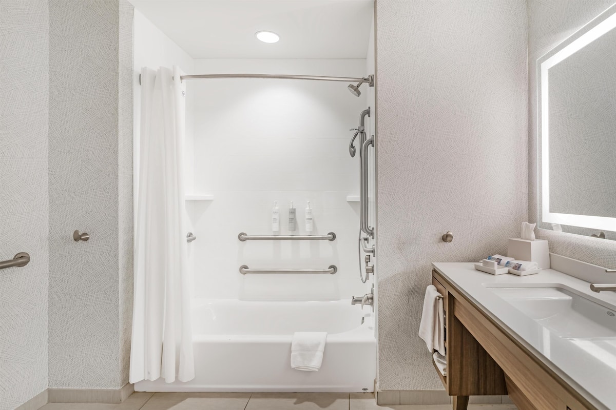 Een moderne badkamer met douche, toilet en wastafel, voorzien van handgrepen en een handdoekrek.