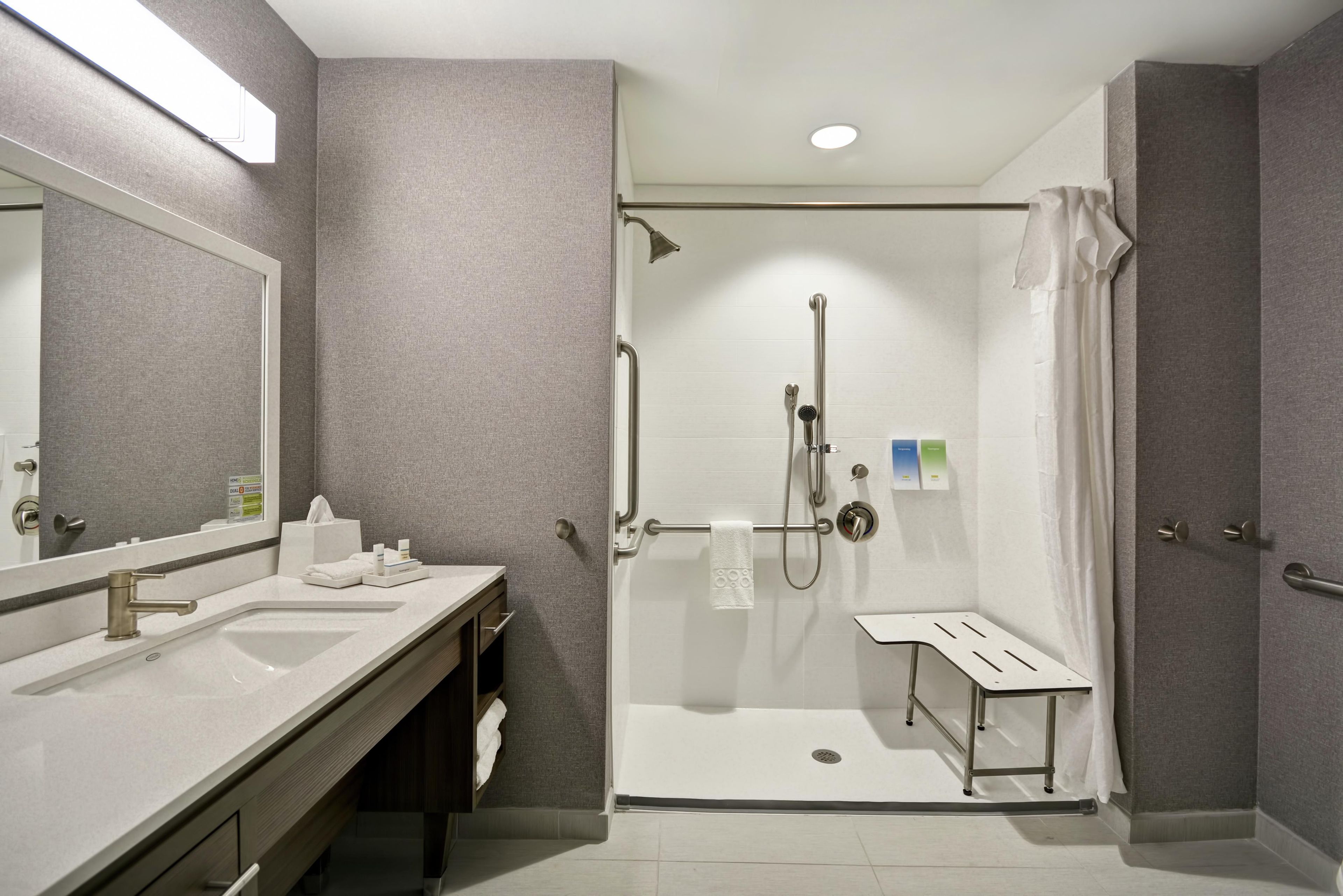 A modern bathroom with a walk-in shower, a vanity with a mirror, and a small bench.