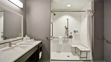 A modern bathroom with a walk-in shower, a vanity with a mirror, and a small bench.