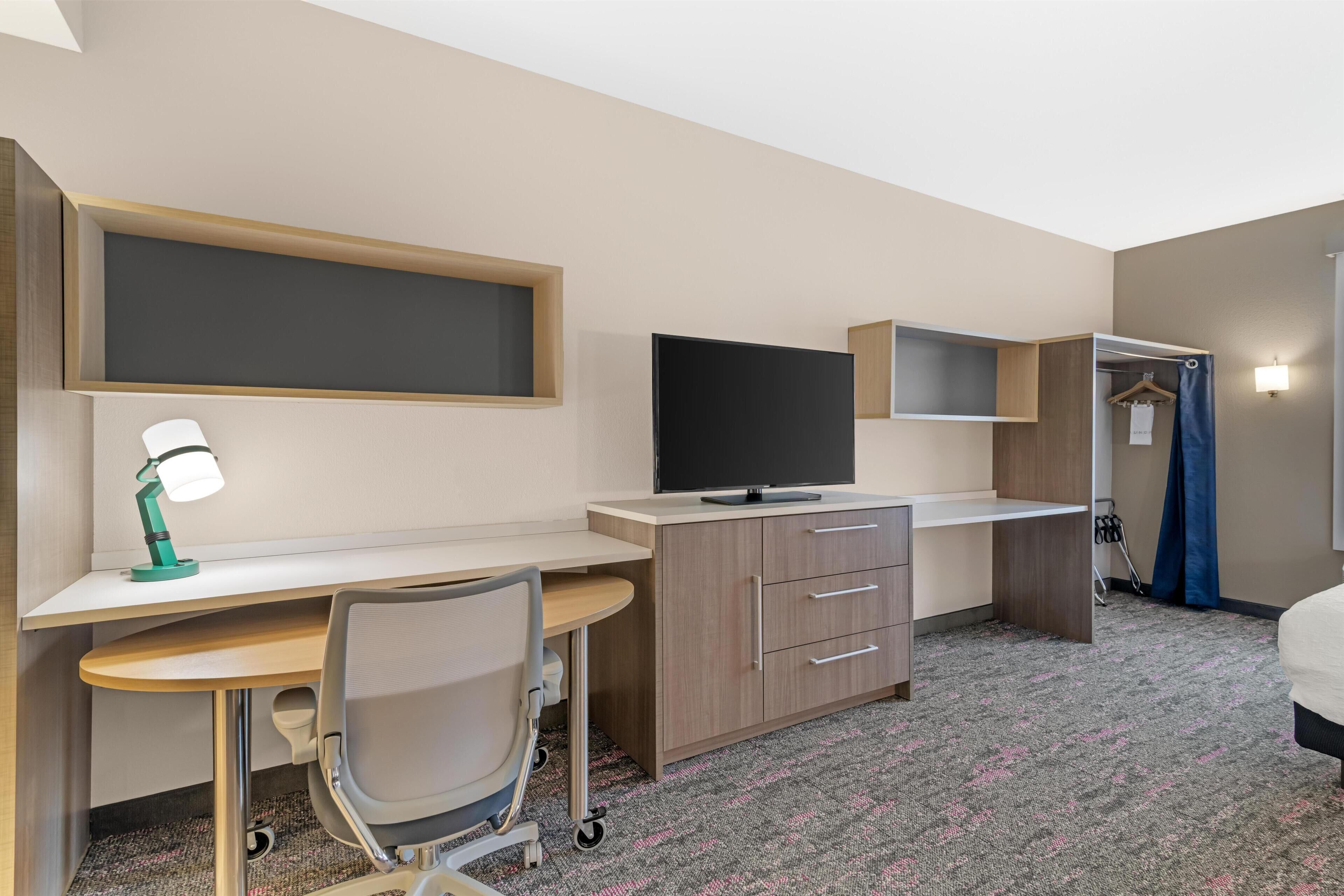 A hotel room with a desk, chair, television, wardrobe, and a bed.