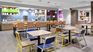 A modern cafeteria with multiple tables and chairs, a counter with a 'Good Morning' sign, and a 'Conserve' energy label. - Home2 Suites by Hilton Orlando South Park (Orlando)