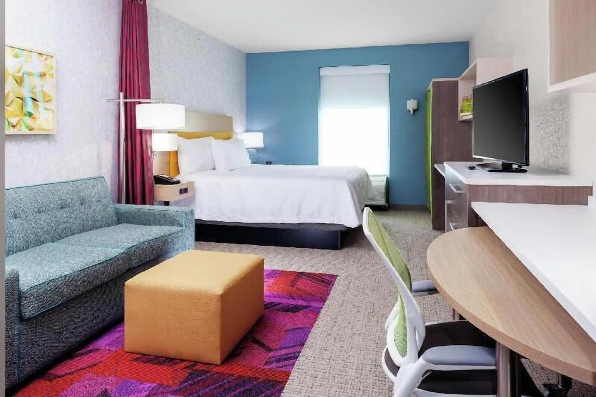 A hotel room with a bed, a sofa, a desk, a TV, and a window.