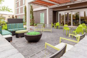 Un espace extérieur aménagé avec des meubles en osier, un grand bac à plantes et un bâtiment doté de grandes fenêtres.