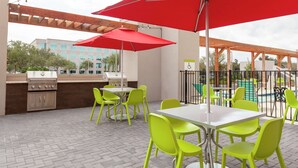 An outdoor patio with a grill, bright green chairs, and a red umbrella. - Home2 Suites by Hilton Orlando South Park (Orlando)