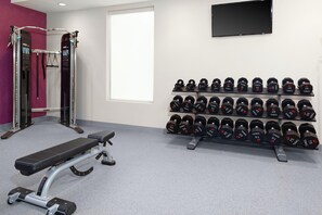 A gym with weightlifting equipment, dumbbells, and a bench. - Home2 Suites by Hilton Orlando South Park (Orlando)