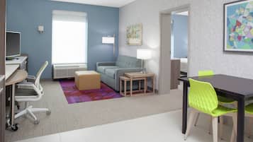 A modern hotel room with a desk, chair, sofa, and a dining area with a table and chairs.