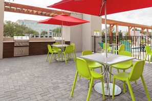 Une terrasse extérieure équipée d’un barbecue, de tables, de chaises et de parasols.