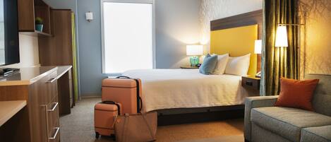 A hotel room with a bed, a sofa, a desk, and a suitcase.