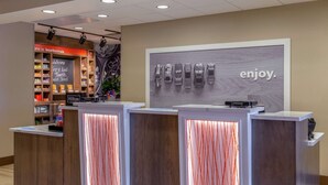 A hotel reception area with a modern design, featuring a reception desk, a wall with a vehicle display, and a sign that reads "enjoy." - Hampton Inn Bourbonnais Kankakee (Bourbonnais)