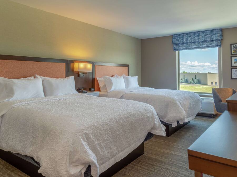 Habitación de hotel con dos camas, un escritorio y una ventana con vistas al exterior.