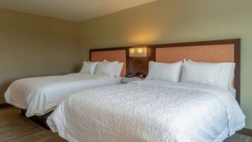 Habitación de hotel con dos camas, cada una con ropa de cama blanca y cabeceros con lámparas.