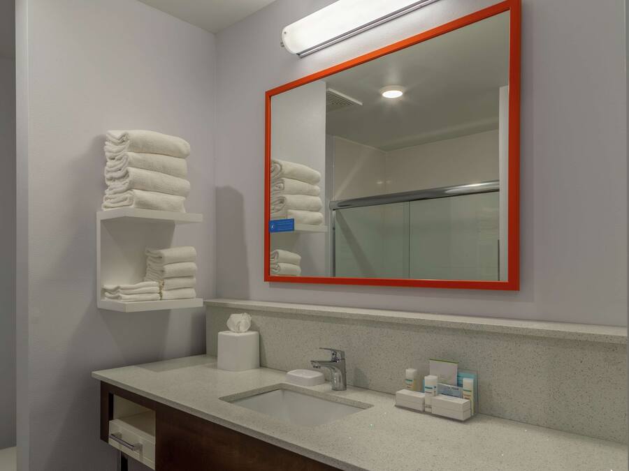 A bathroom with a sink, mirror, towel rack, and toiletries.